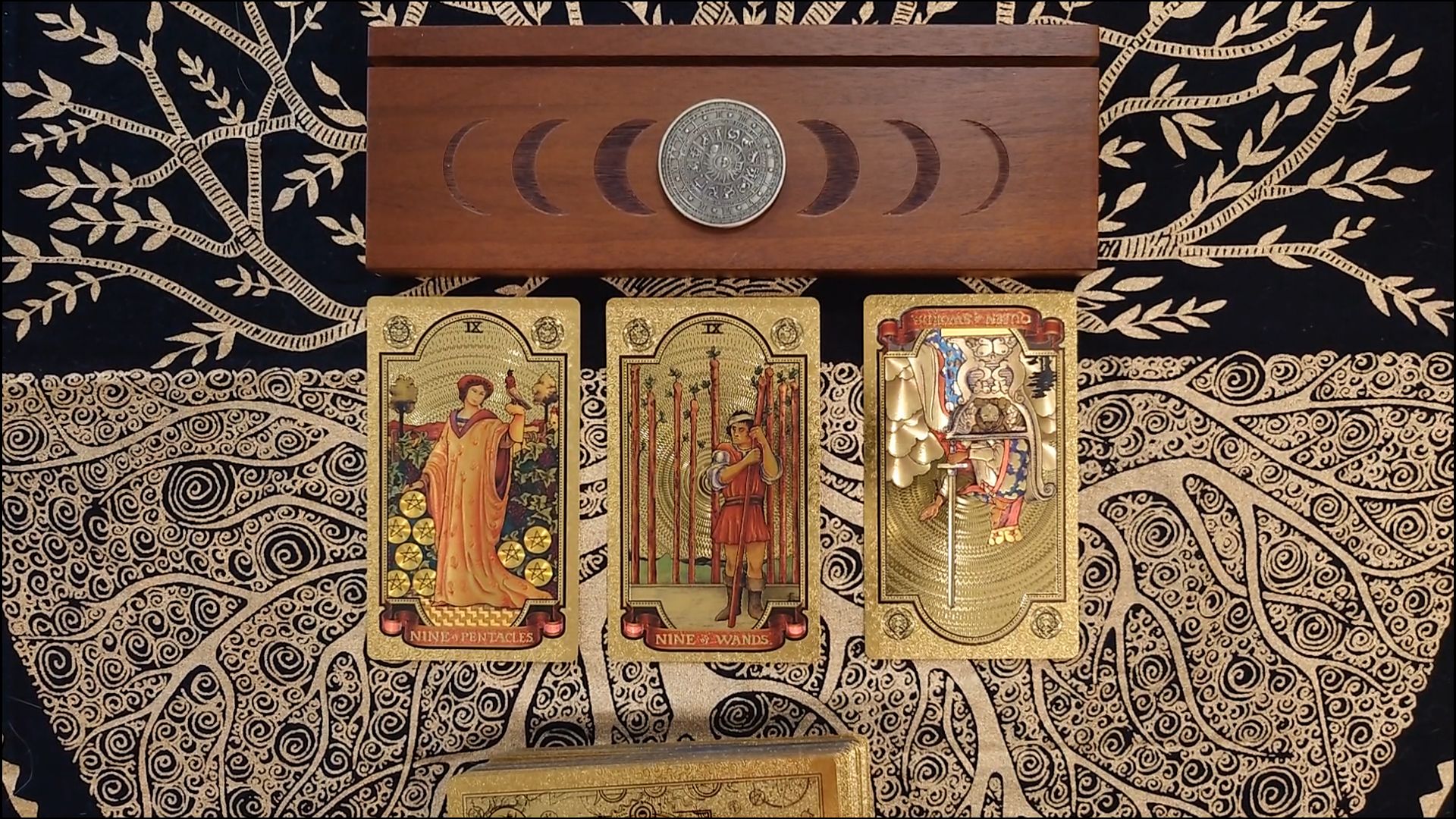Nine of Pentacles, Nine of Wands, and Queen of Swords (reversed) from the Piedmontese tarot deck, laid out on a gold and black patterned cloth beneath a crescent moon altar box.